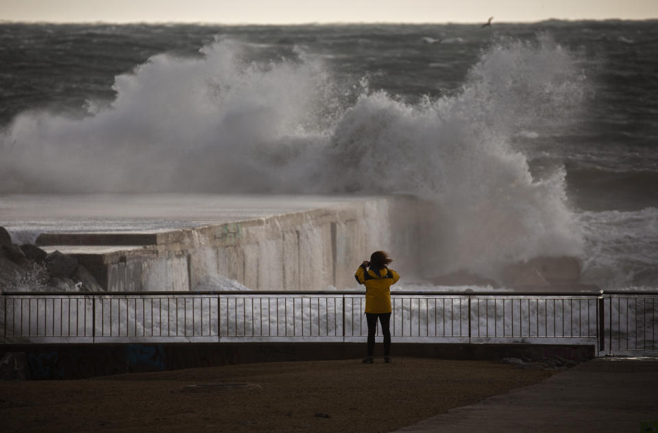 A woman photographs the Mediterranean sea during strong winds in Barcelona, Spain, Monday, Jan. 20, 2020. Two people have died as storms carrying heavy snowfalls and gale-force winds lashed many parts of Spain on Monday. The storm has forced the closure of Alicante airport and some 30 roads in eastern region. Six provinces are on top alert. (AP Photo/Emilio Morenatti)