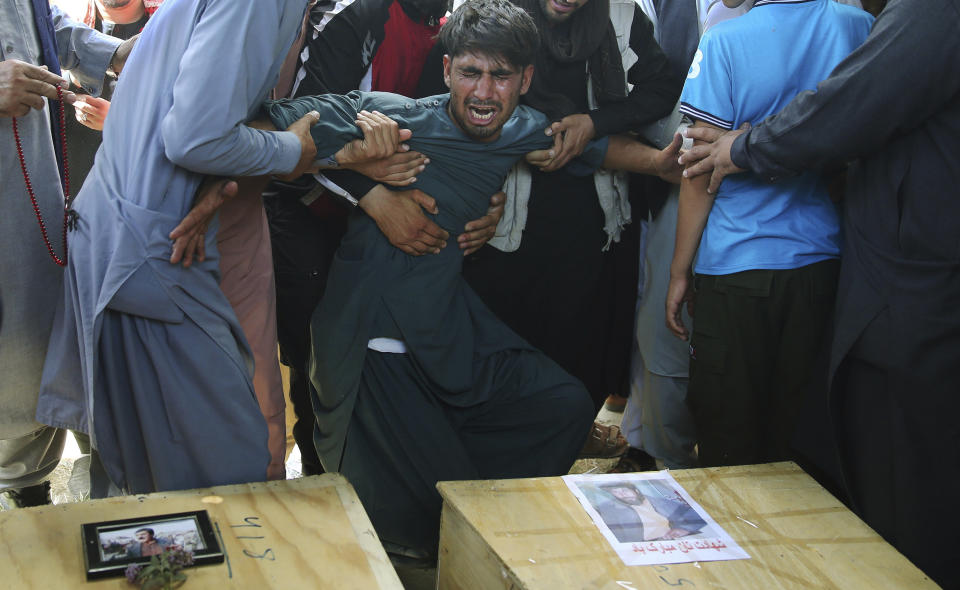 FILE - In this Aug. 18, 2019 file photo, men hold back a grieving relative next to the coffins of victims of a wedding hall bombing during a mass funeral in Kabul, Afghanistan. A new survey released by the Asia Foundation Tuesday, Dec. 3, 2019, says Afghans are increasingly fearful for their personal safety, but slightly more believe their war-weary country is moving in the right direction compared to previous years. (AP Photo/Rafiq Maqbool, File)