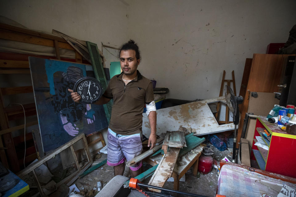 Hasan Al Armali, holds a wall clock that was stoped working at the time of the Tuesday's explosion in the seaport of Beirut, poses for a photograph at his bedroom inside his destroyed apartment, in Beirut , Lebanon, Thursday, Aug. 6, 2020. The gigantic explosion in Beirut on Tuesday tore through homes, blowing off doors and windows, toppling cupboards, and sent flying books, shelves, lamps and everything else. Within a few tragic seconds, more than a quarter of a million people of the Lebanese capital's residents were left with homes unfit to live in. Around 6,200 buildings are estimated to be damaged. (AP Photo/Hassan Ammar)