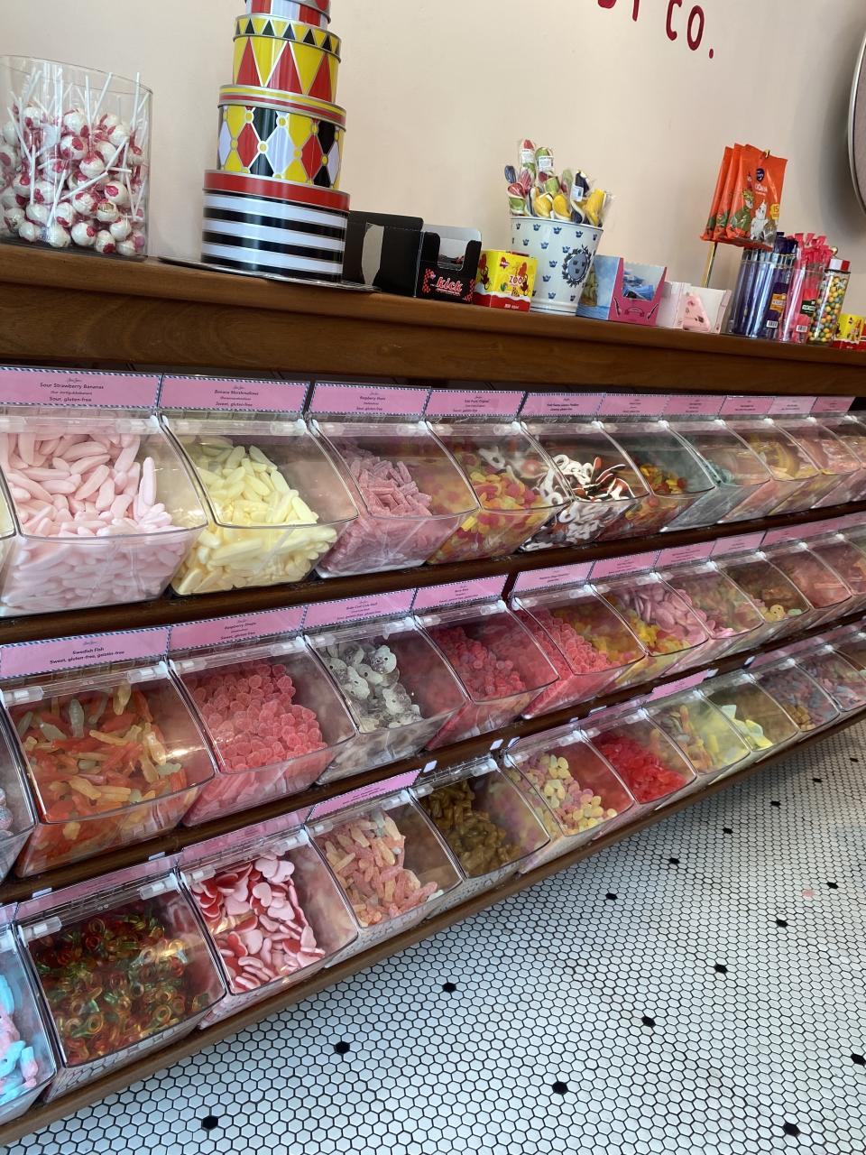 Candy store display with various types of colorful sweets in clear bins on shelves, and decorative items on top