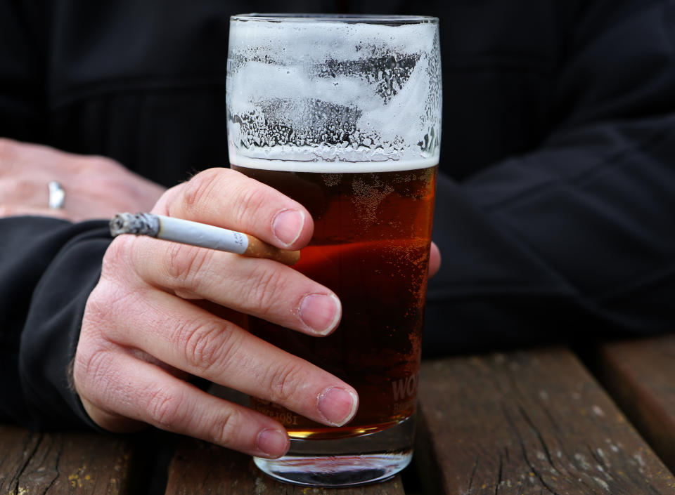 A man holds a cigarette and a pint of beer.