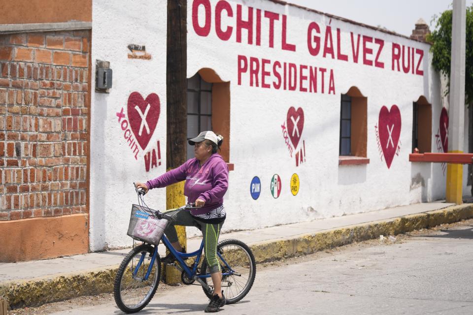 Una mujer pasa en bicicleta por delante de un mural político que promueve a la candidata presidencial Xóchitl Gálvez, en su ciudad natal en Tepatepec, México, el viernes 10 de mayo de 2024. Gálvez vendió tamales de niña en esa pequeña ciudad del centro de México; después dio el salto a la política nacional. (AP Foto/Fernando Llano)