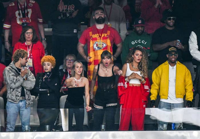 Group of seven people stands at a sporting event. Notable: Ice Spice, Sophie Turner, Taylor Swift and Blake Lively each wore outfits ranging from casual to stylish