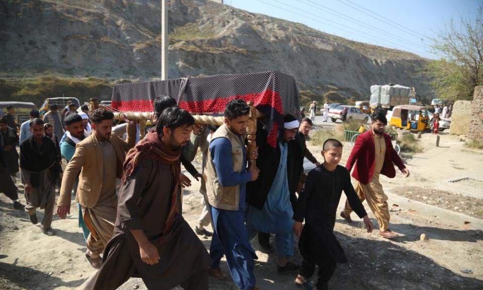 A group of Afghan pallbearers carry a coffin covered in a drape across rough ground with a line of mountains in the background