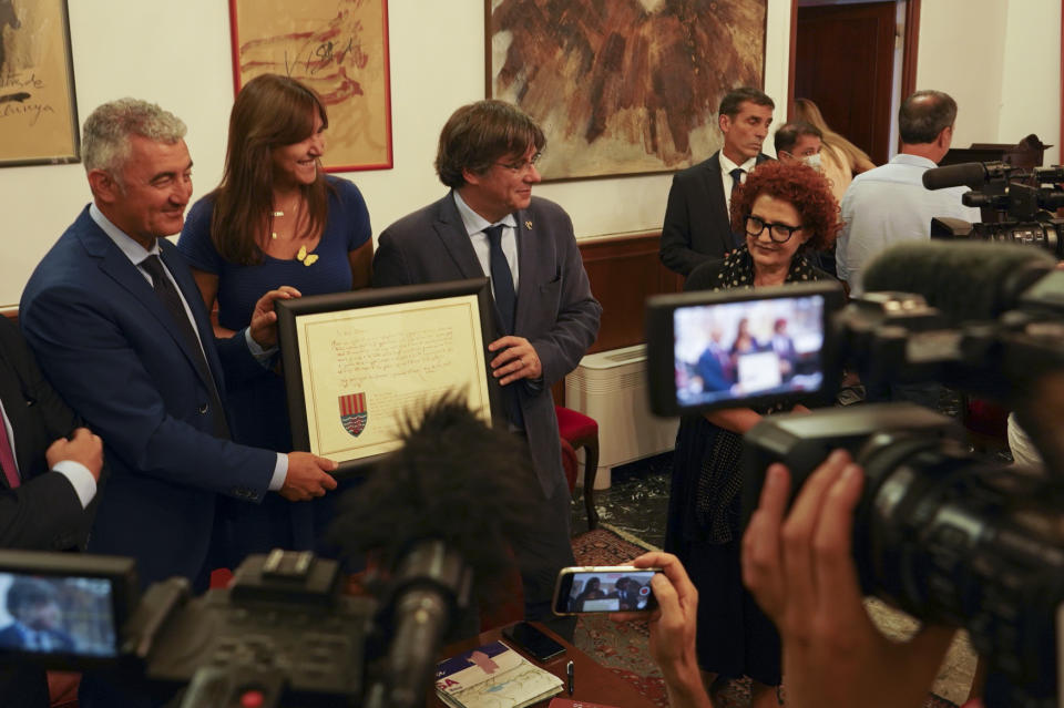 Catalan separatist leader Carles Puigdemont, right, flanked by Speaker of the Catalan Parliament Laura Borras exchanges gifts with Mayor of Alghero Mario Conoci, left, in Alghero, Sardinia, Italy, Saturday, Sept. 25, 2021. Puigdemont was visiting the city hall after he took a leisurely walk in the Sardinian city, waving to supporters, a day after a judge freed him from jail pending a hearing on his extradition to Spain, where the political firebrand is wanted for sedition. (AP Photo/Andrea Rosa)