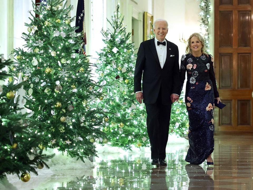 Joe Biden and Jill Biden walk by Christmas trees in the White House