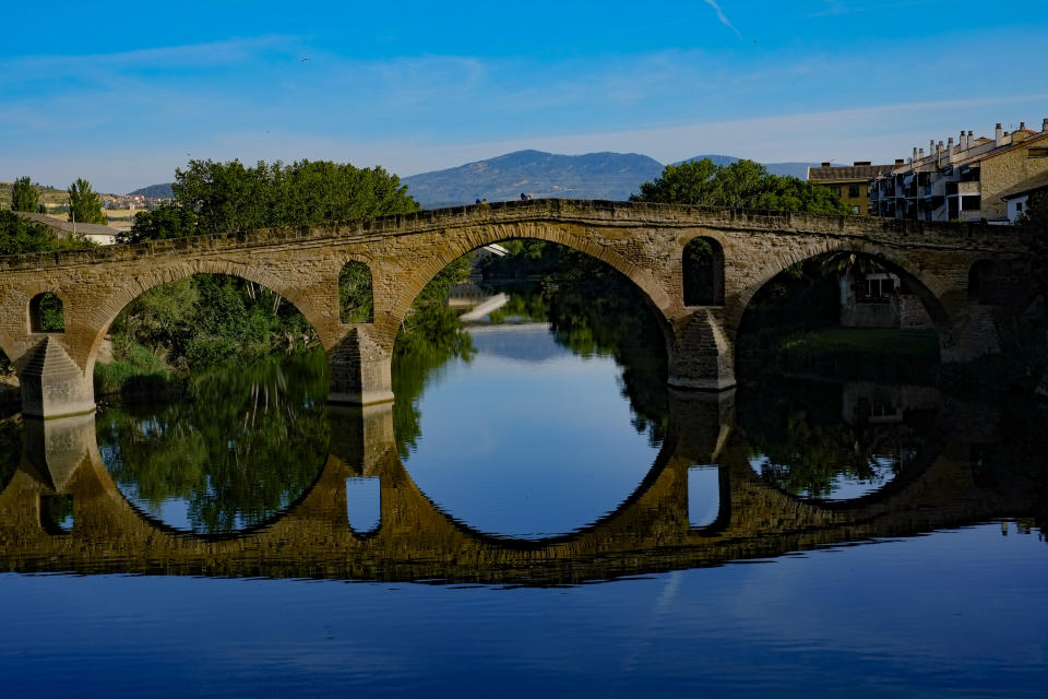 Peregrinos cruzan un puente durante una etapa del "Camino de Santiago" en Puente La Reina, en el norte de España, el martes 31 de mayo de 2022. (AP Foto/Alvaro Barrientos)