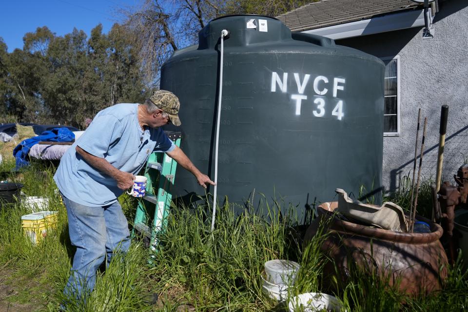 Fred Imfeld points to the level on his water tank Sunday, March 17, 2024, in Corning, Calif. Imfeld and his wife have a dried up well, so they get a 2,500-gallon tank filled with water a few times a month for their needs. They also get potable water delivered as the couple tries to save to drill a new well. (AP Photo/Godofredo A. Vásquez)