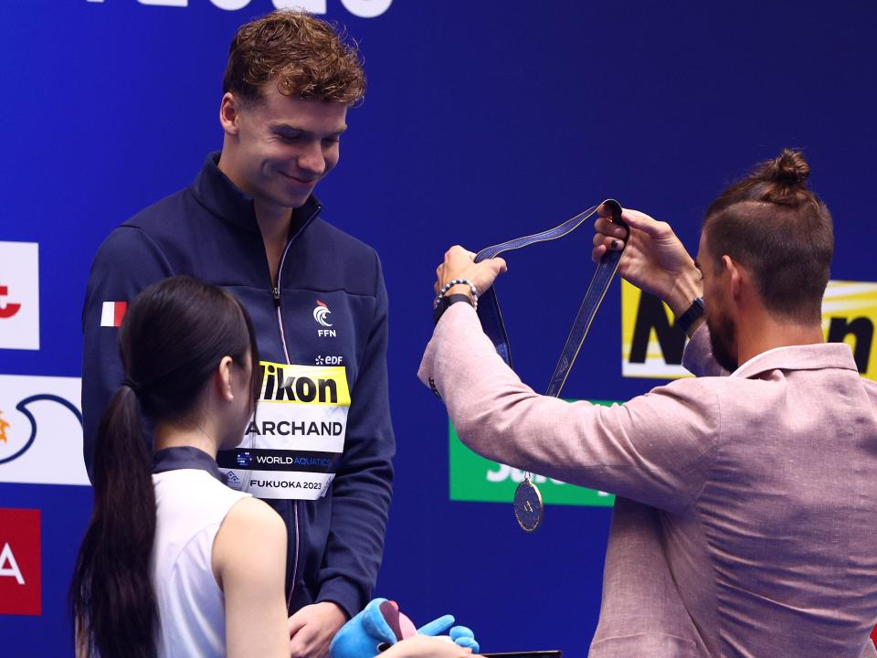 Léon Marchand being presented with his gold medal by Michael Phelps.