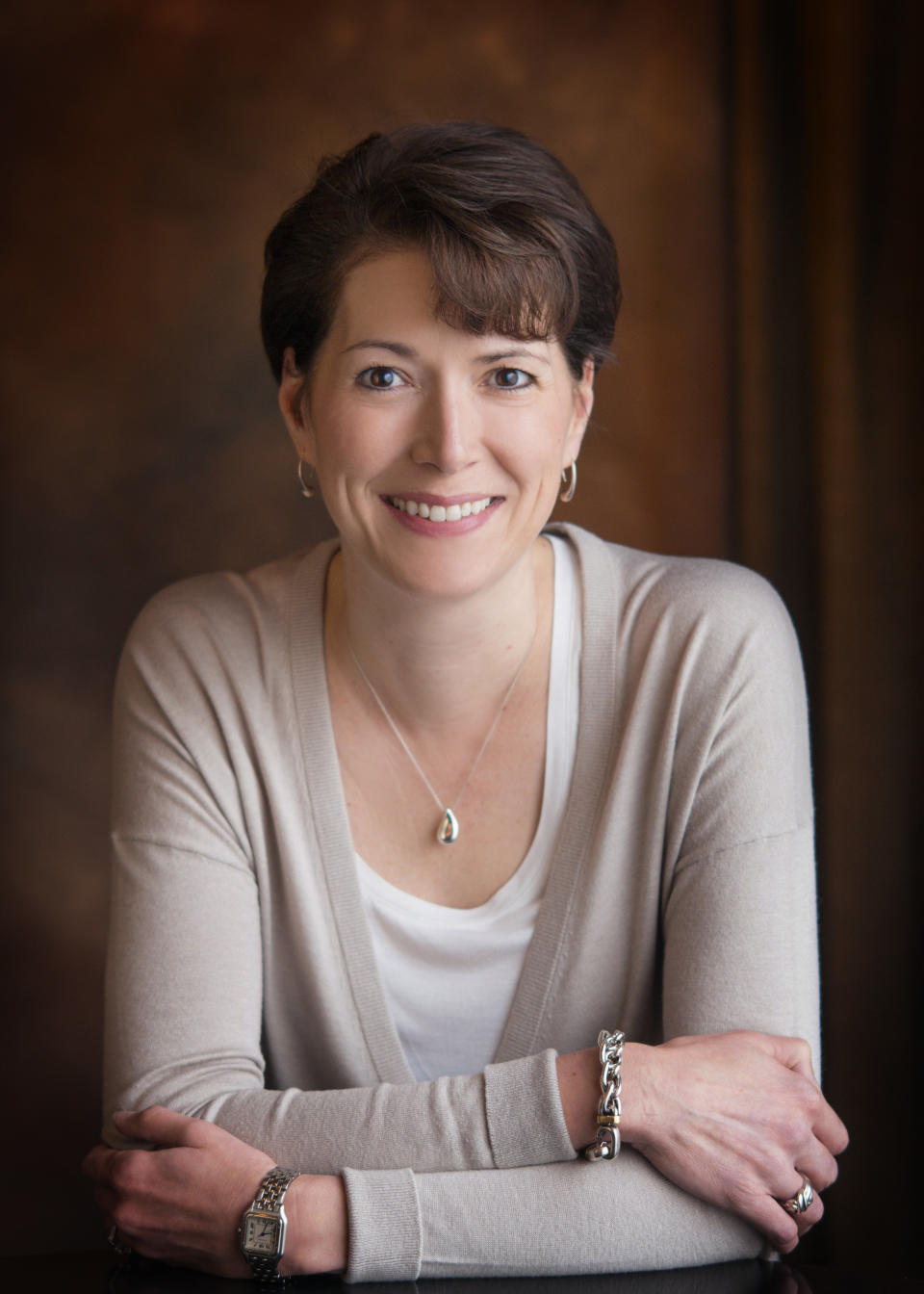 Woman in a light top with a necklace, smiling at the camera with her arms crossed