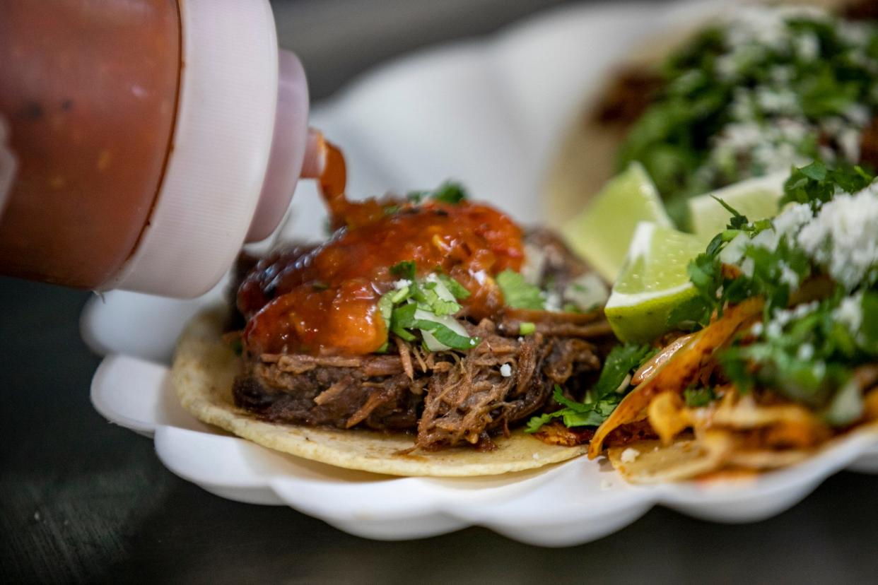 Diana Gomez finishes a braised brisket taco with her homemade salsa while serving dinner at Taco Hernandez food truck parked in front of Next Chapter Books for poetry night in Detroit on Thursday, Feb. 15, 2024.