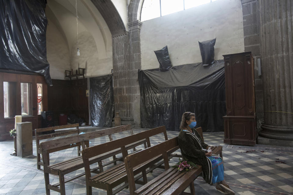 A devotee sits inside the Our Lady of the Angels Catholic parish where black tarps protect religious statues, during a restoration of the building that was damaged in an earthquake five years ago, in Mexico City, Sunday, Aug. 7, 2022. Just weeks before the anniversary of the Sept. 19, 2017, quake, Rev. Adrian Vazquez announced to his parishioners that restoration work was resuming on the Catholic temple, which houses a treasured painting of the Assumption of the Virgin considered miraculous for having survived floods and earthquakes. (AP Photo/Ginnette Riquelme)