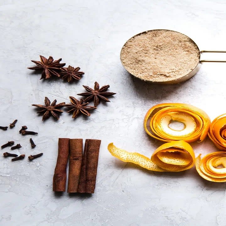 Star anise, cloves, cinnamon sticks, brown sugar, orange peels, cider, and wine on a table