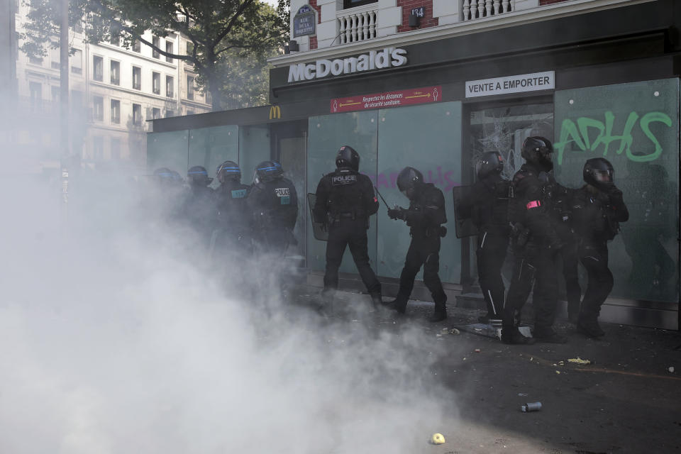 Riot police officers take positions in front of the smashed window of a restaurant with a tag reading "Anticapitalist" during a May Day demonstration march from Republique, Bastille to Nation, in Paris, France, Sunday, May 1, 2022. Citizens and trade unions in France take to the streets to put out protest messages to their governments as a rallying cry against newly reelected President Emmanuel Macron. (AP Photo/Lewis Joly)