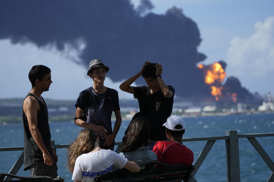 Youth gather on a dock while flames and smoke continue to rise from the Matanzas Supertanker Base, as firefighters and specialists work to quell the blaze which began during a thunderstorm the night before, in Matazanas, Cuba, Saturday, Aug. 6, 2022. Cuban authorities say lightning struck a crude oil storage tank at the base, causing a fire that led to four explosions which injured dozens. (AP Photo/Ramon Espinosa)