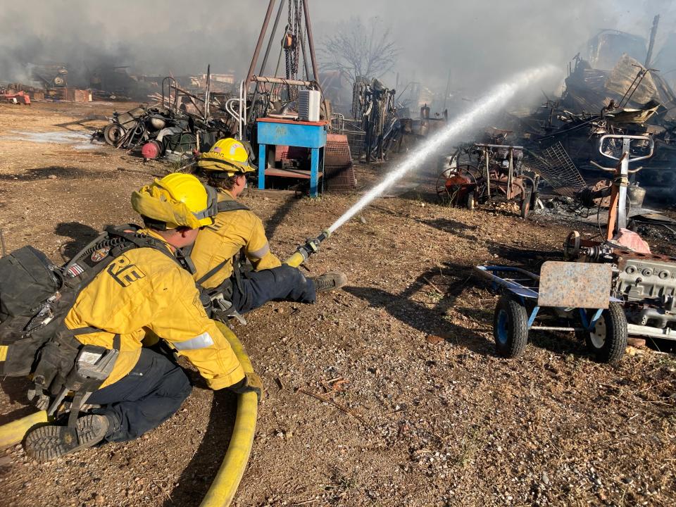 Firefighters hose down a shop off Spring Gulch Road north of Anderson that was destroyed in the Peter Pan Fire on Thursday.