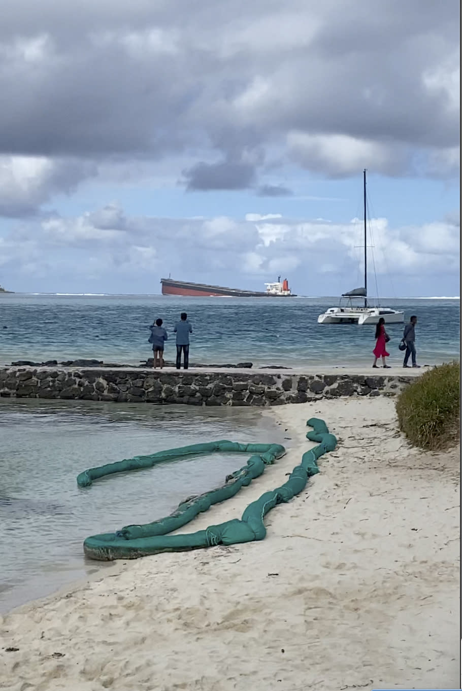 In this still image taken from video provided by Grégoire Rouxel, people watch a ship that ran aground offshore that is leaking fuel, Friday, Aug. 7, 2020, in Mauritius. The Indian Ocean island of Mauritius has declared a "state of environmental emergency" after a Japanese-owned ship that ran aground offshore days ago began spilling tons of fuel. Prime Minister Pravind Jugnauth announced the development late Friday, as satellite images showed a dark slick spreading near environmental areas the government called "very sensitive." (@gregrouxel via AP)