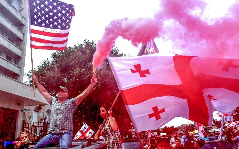 Protesters celebrate with American and Georgian flags after the head of the ruling party said next year's elections would be held under a proportional system - AFP