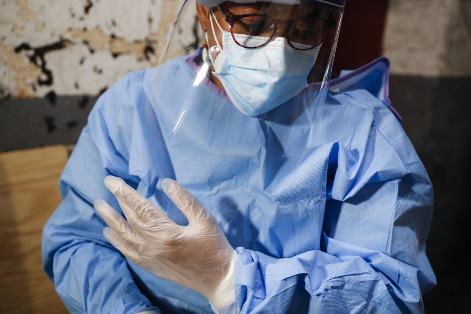 In this Thursday, April 23, 2020 photo, Ruth Caballero, a nurse with The Visiting Nurse Service of New York, suits up in protective equipment before treating a COVID-19 patient on her rounds in upper Manhattan in New York. Home care nurses, aides and attendants, who normally help an estimated 12 million Americans with everything from bathing to IV medications, are now taking on the difficult and potentially dangerous task of caring for coronavirus patients. (AP Photo/John Minchillo)