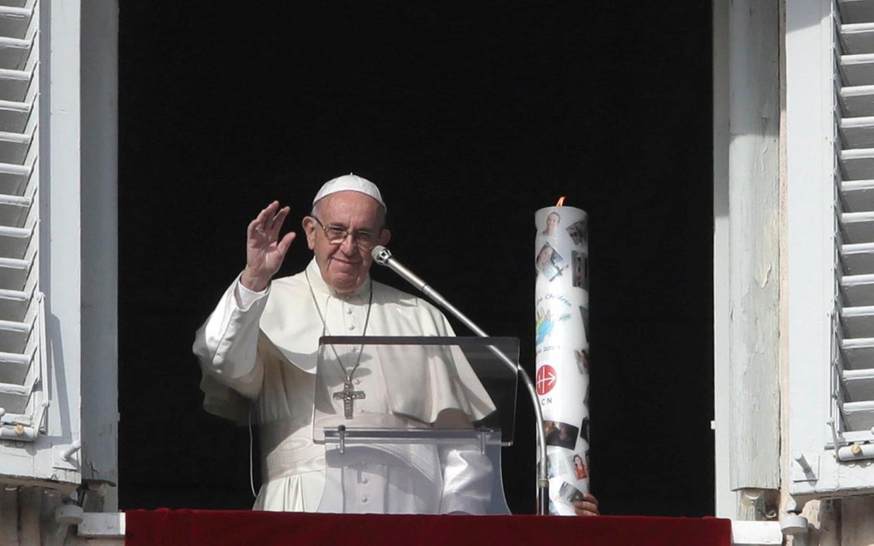 A candle decorated with the faces of Syrian children suffering from war is placed next to Pope Francis during the Angelus noon prayer on Sunday 2 December - AP