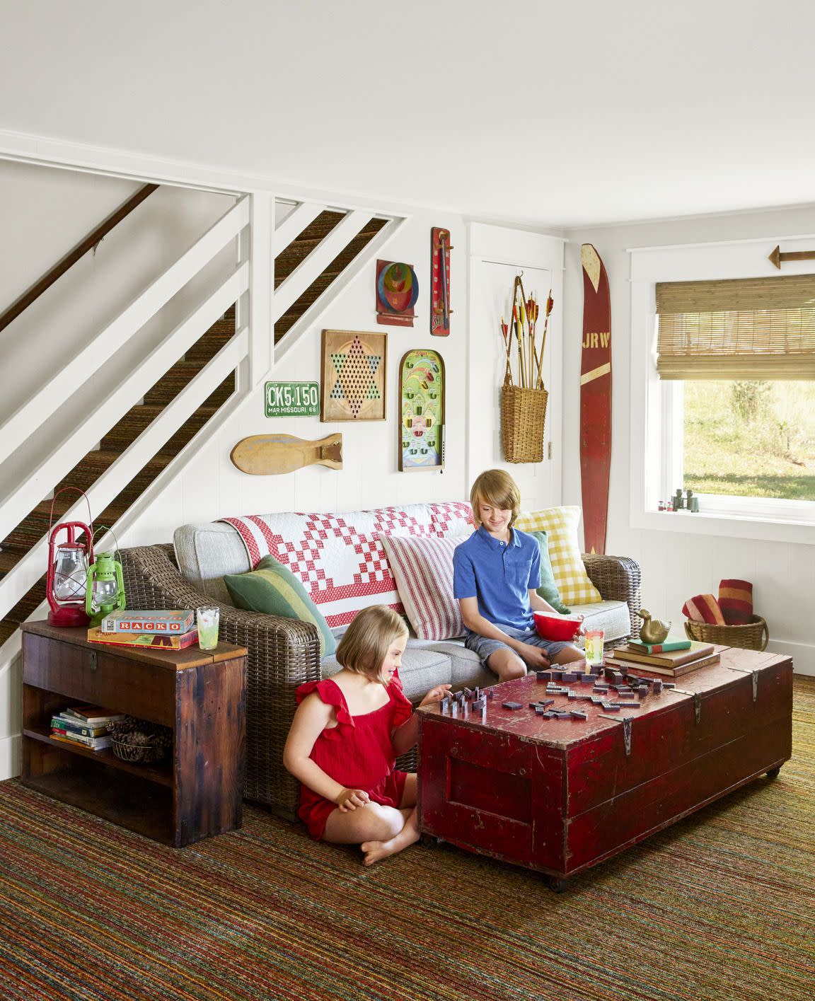 nostalgic lake cabin family room with colorful carpet, wicker sofa, red coffee table, and vintage games on the wall