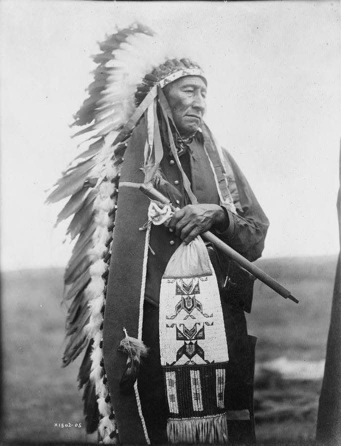 Three-quarter length portrait of Chief Stinking Bear, a Dakota man wearing a feathered headdress.