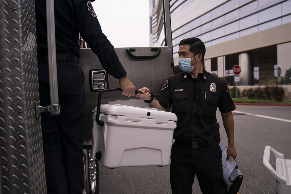 Torrance fire Capt. John Kubota, right, hands a cooler containing the Pfizer COVID-19 vaccine to Alessandro Demuro as they prepare to inoculate two sisters who have muscular dystrophy, at their home, Wednesday, May 12, 2021, in Torrance, Calif. Teamed up with the Torrance Fire Department, Torrance Memorial Medical Center started inoculating people at home in March, identifying people through a city hotline, county health department, senior centers and doctor's offices, said Mei Tsai, the pharmacist who coordinates the program. (AP Photo/Jae C. Hong)