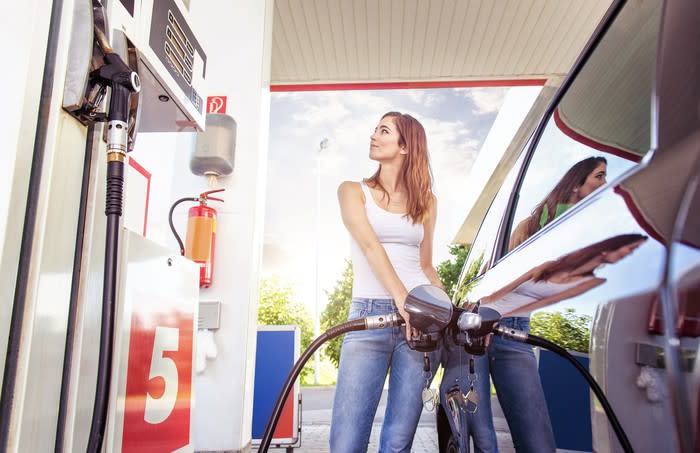 A young woman refuels her car at a gas station.