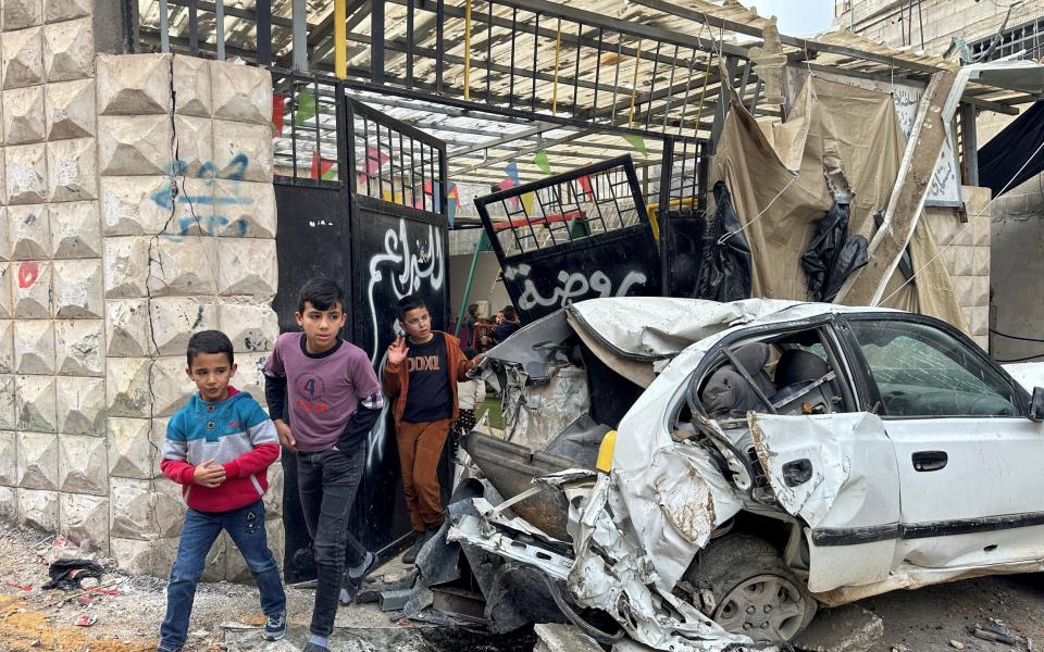 Palestinian children walk near a damaged car following an Israeli raid on Tulkarm in the occupied West Bank