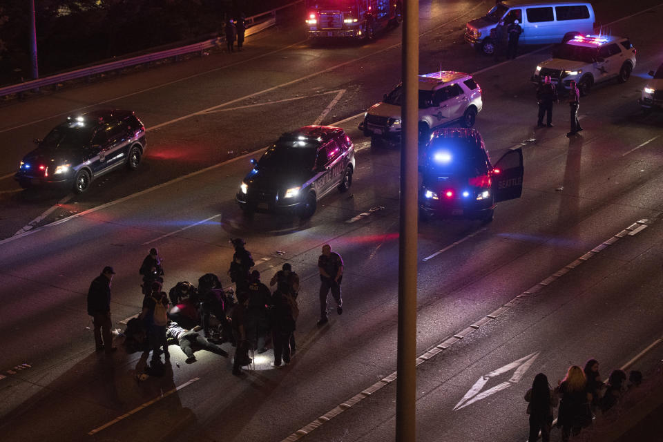 Emergency workers tend to an injured person on the ground after a driver sped through a protest-related closure on the Interstate 5 freeway in Seattle, authorities said early Saturday, July 4, 2020. Dawit Kelete, 27, has been arrested and booked on two counts of vehicular assault. (James Anderson via AP)