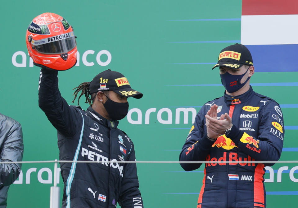 Mercedes driver Lewis Hamilton of Britain holding the helmet of former F1 legend Michael Schumacher, celebrates after winning the Eifel Formula One Grand Prix at the Nuerburgring racetrack in Nuerburg, Germany, as Red Bull driver Max Verstappen of the Netherlands, right who finished second applauds him at the podium, Sunday, Oct. 11, 2020. Hamilton with this win equals 91 wins in F1 races as Michael Schumacher. Renault driver Daniel Ricciardo of Australia finished third. (Ronald Wittek, Pool via AP)