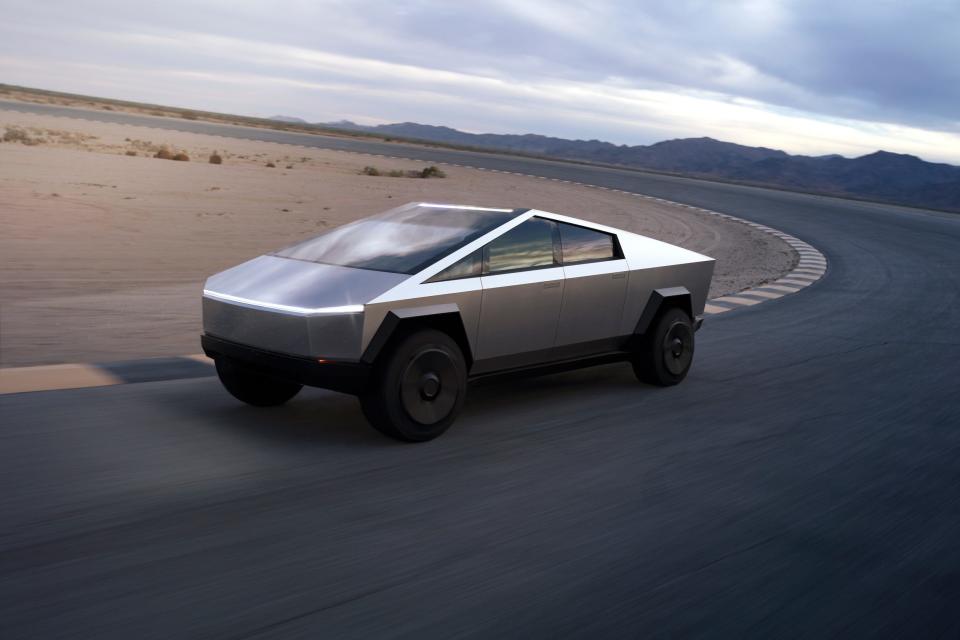 The Tesla Cybertruck drives on a test track, with mountains in the background. 