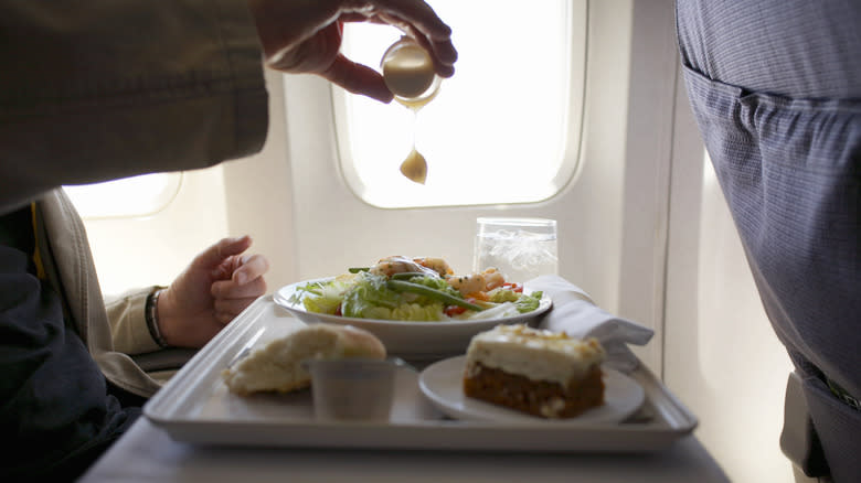 Person on airplane dressing salad
