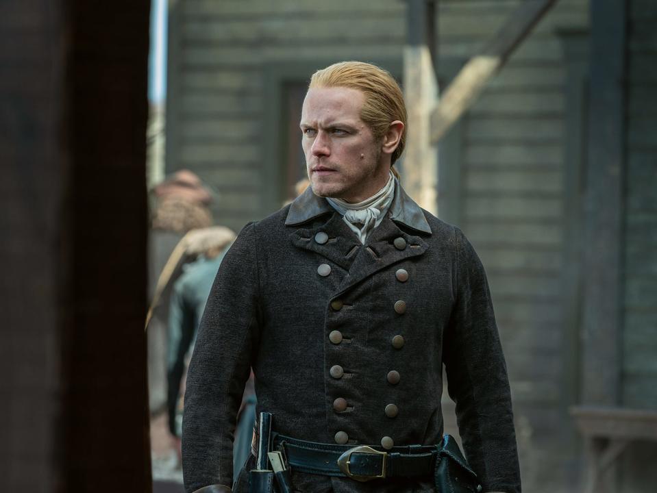 Jamie Fraser wearing a black coat and looking off to the left with an intense expression.