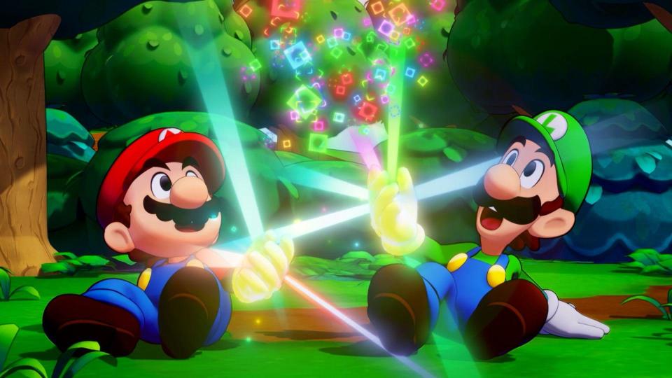 Mario and Luigi, wearing their famous blue overalls and coloured caps, sit on the ground. Each is looking upwards with a shocked expression as a magical yellow glow emanates from their hand, creating a cascade of colourful squares between them.