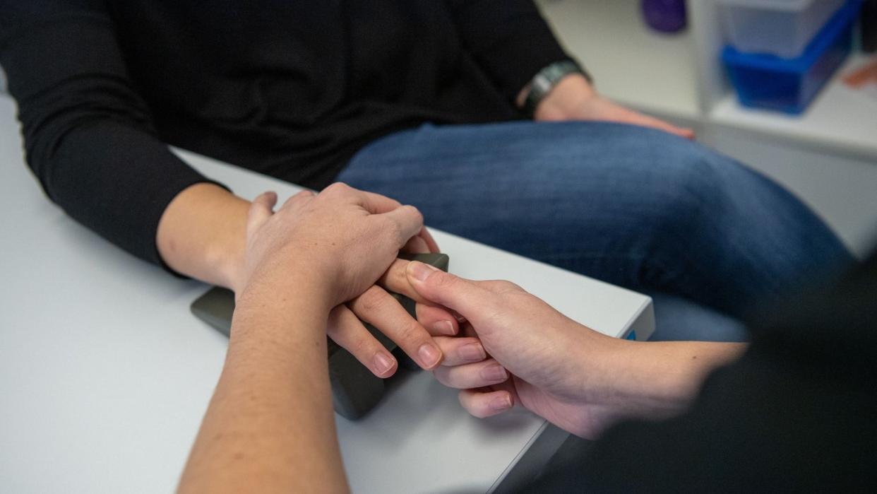 Eine Ergotherapeutin massiert einer Frau während einer Handtherapie einen Finger. Foto: Lino Mirgeler/Illustration