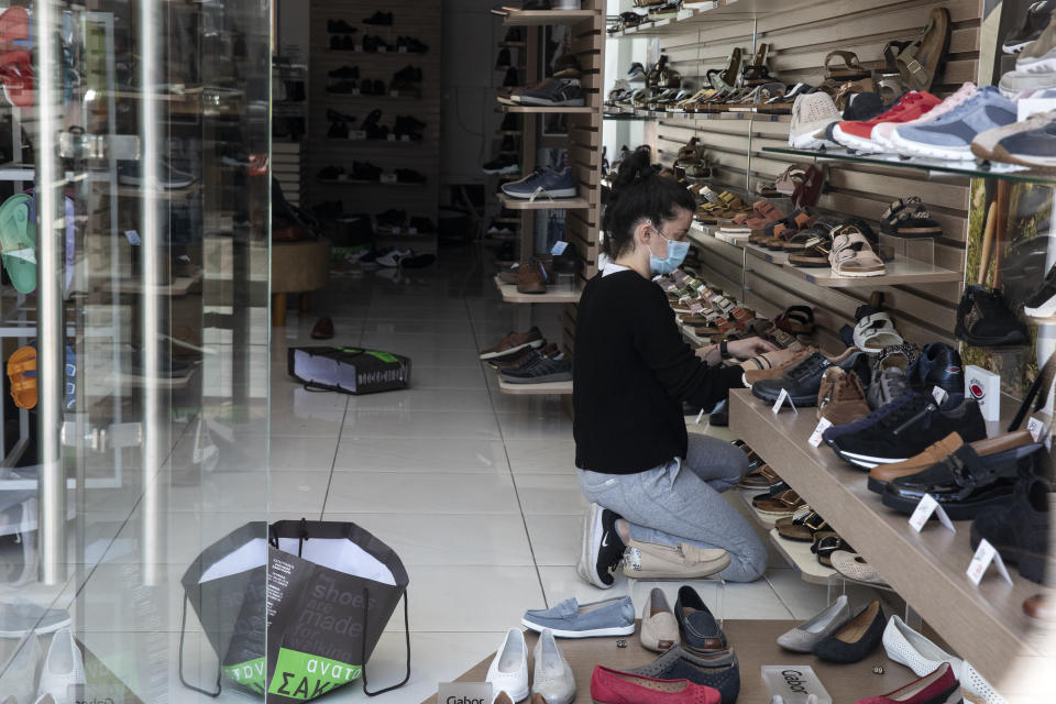 An employee, wearing a face mask to curb the spread of the coronavirus, adjusts shoes inside a shop, at Glyfada suburb west of Athens, Saturday, April 3, 2021. Greece has relaxed some coronavirus restrictions despite surging COVID-19 cases that are straining hospitals to their limits, with retail stores to reopen and people allowed to drive outside their home municipalities for exercise on weekends. (AP Photo/Yorgos Karahalis)