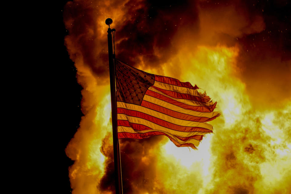 A flag flies over a department of corrections building ablaze during protests, late Monday, Aug. 24, 2020, in Kenosha, Wis., sparked by the shooting of Jacob Blake by a Kenosha Police officer a day earlier. (AP Photo/Morry Gash)
