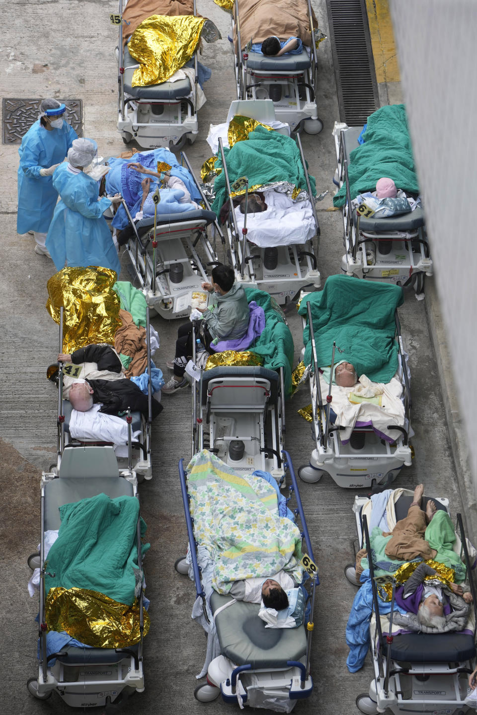 Patients lie on hospital beds as they wait at a temporary holding area outside Caritas Medical Centre in Hong Kong Wednesday, Feb. 16, 2022. There was visible evidence that Hong Kong hospitals were becoming overwhelmed by the latest COVID surge, with patients on stretchers and in tents being seen to by medical personnel on Wednesday outside the Caritas hospital. (AP Photo Vincent Yu)