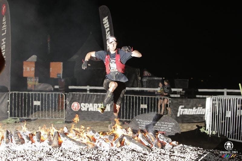 Elite performance scientist Andrew Herr competing in a Spartan race obstacle course leaping over flames