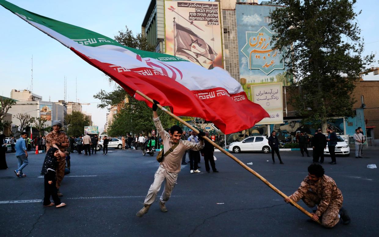 Demonstrators wave a huge Iranian flag backdropped by a building emblazoned with anti-Israeli messages, in Tehran, Iran