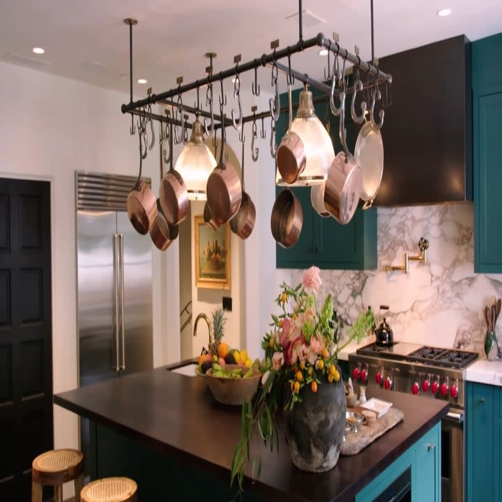 The kitchen has pots and pans hanging overhead and the cabinets are green and there is an island