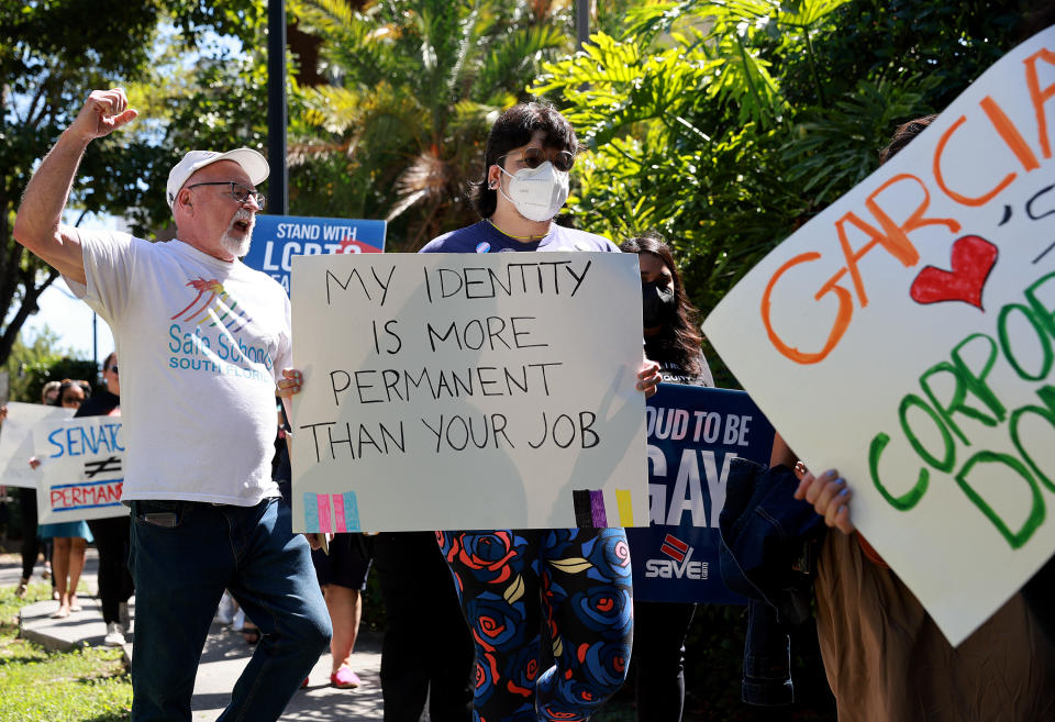 Protesters in Miami holding signs, one of which reads: My identity is more permanent than you job.