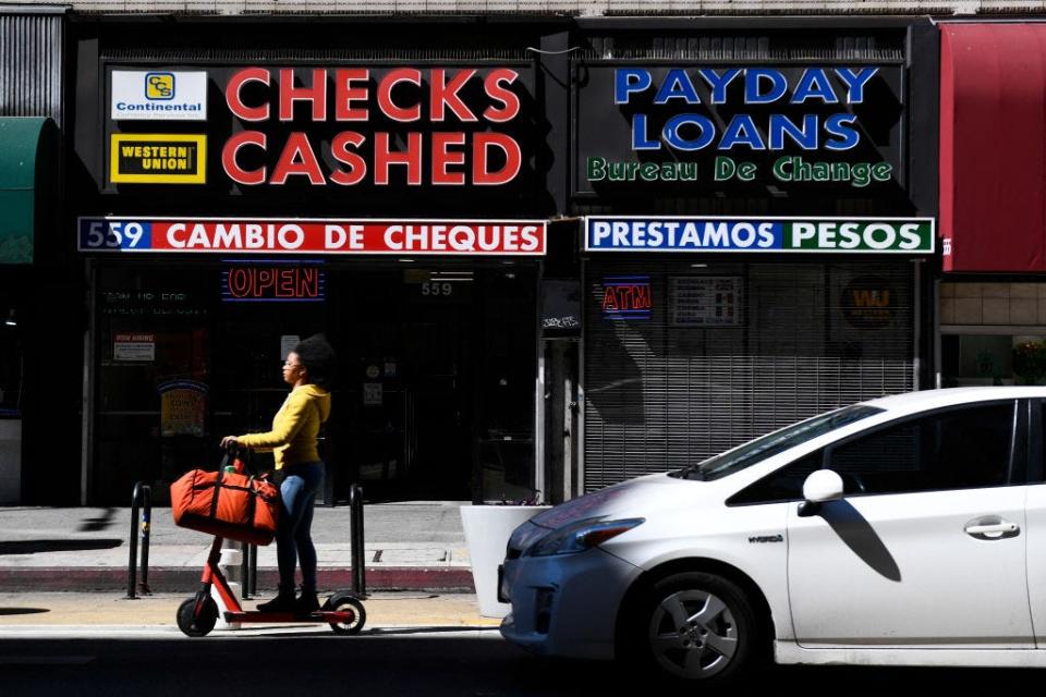 A person rides a scooter past a check cashing and payday loans store on March 11, 2022, in downtown Los Angeles.