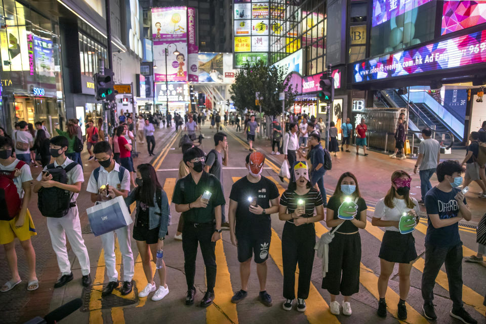 Protestors wearing masks stand along a commercial shopping street in Hong Kong, Friday, Oct. 18, 2019. Hong Kong pro-democracy protesters are donning cartoon and superhero masks as they formed a human chain across the semiautonomous Chinese city, in defiance of a government ban on face coverings. (AP Photo/Mark Schiefelbein)