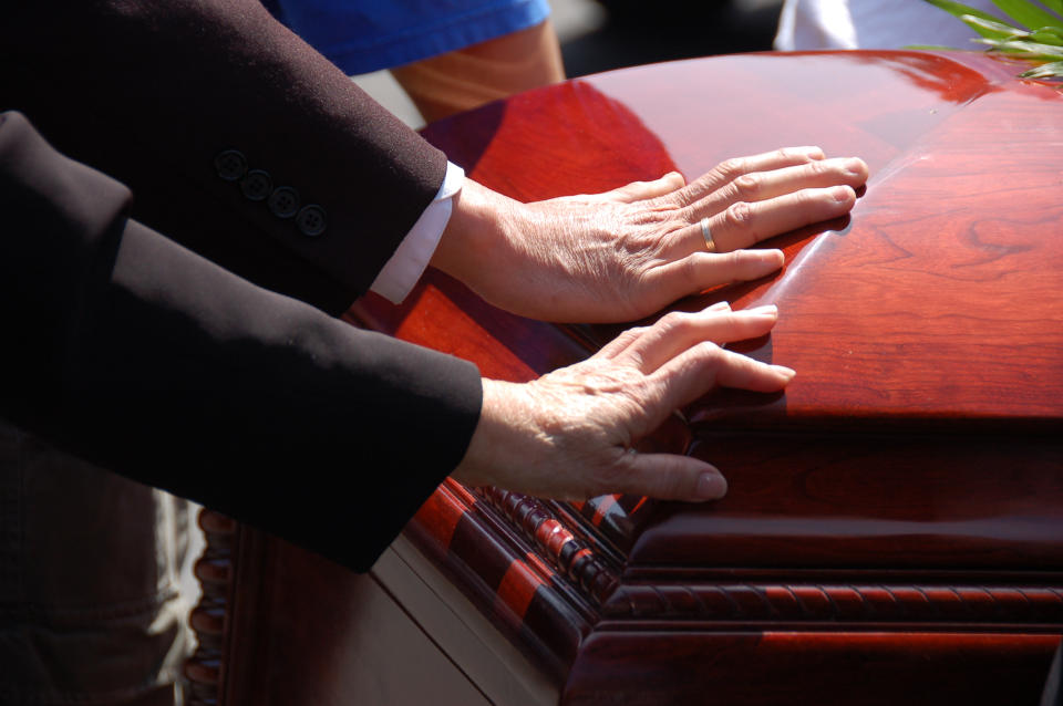 Two hands on a corner of a shiny casket at a funeral