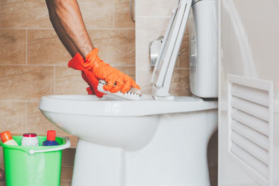 toilet bowl cleaning, hand with orange gloves scrubbing the toilet