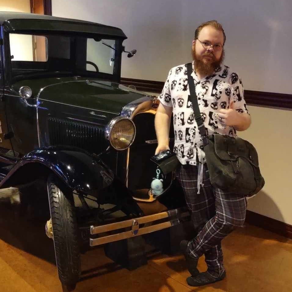 Person standing beside a vintage car holding a bag with a plush toy on it