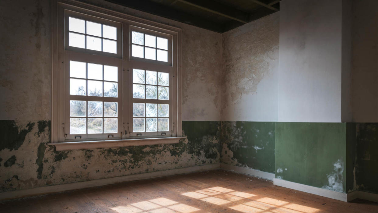  A photograph of an abandoned, old house, showing lighting shining through windows and highlighting a wooden floor. 