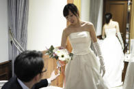 In this April 11, 2019, photo, Kenzo Watanabe, left, passes a bouquet to his fiancee Chiharu Yanagihara as she tries on a wedding dress at a Japanese wedding company in Tokyo. Japan is getting ready for its biggest celebration in years with the advent of the Reiwa era of soon-to-be emperor Naruhito. That means big opportunities for businesses hoping consumers will splash out on long holidays and memorabilia. (AP Photo/Eugene Hoshiko)